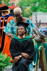 Family member hoods a Methodist University student during a commencement graduation at Segra Stadium