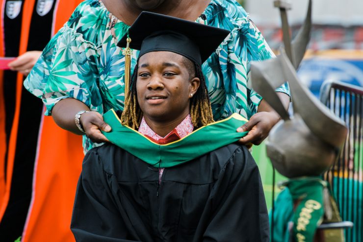 Family member hoods a Methodist University student during a commencement graduation at Segra Stadium