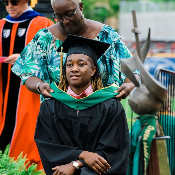 Family member hoods a Methodist University student during a commencement graduation at Segra Stadium