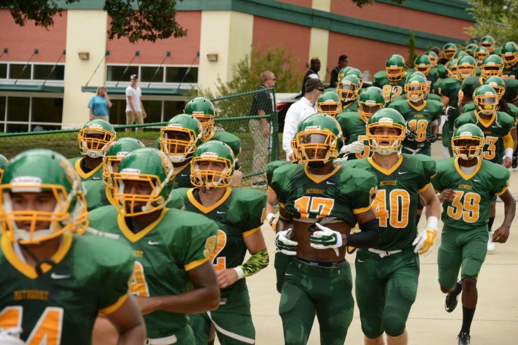 The Monarchs take the field with the Football Fieldhouse in the background