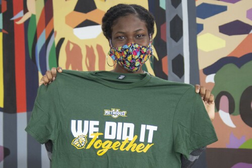 A student holds up a shirt that says "We Did It Together"