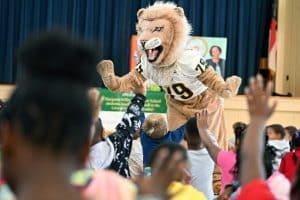 Methodist University mascot, King, embraces a gymnasium filled with young students at Margaret Willis Elementary School during the University's "Love of Literacy" event.