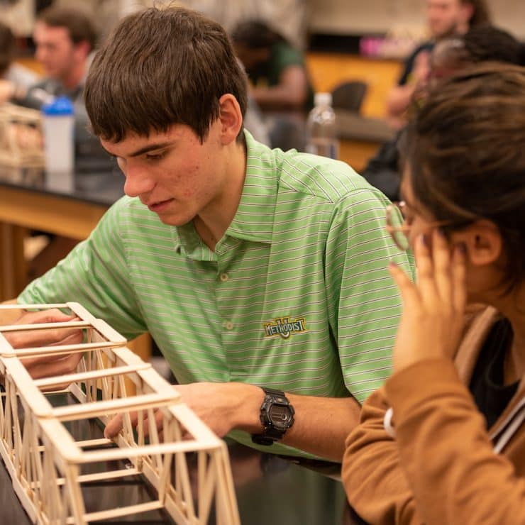 Two Engineering students closely look at the bridge they constructed in class at Methodist University