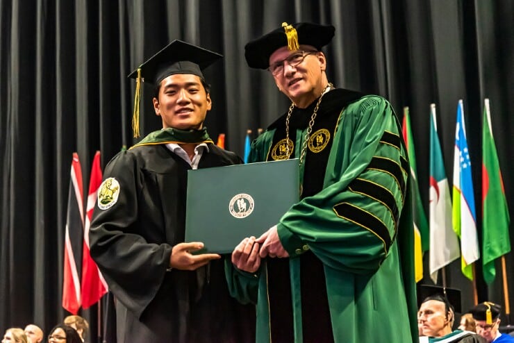 President Stanley T. Wearden (right) stands with new Methodist University graduate Andre Chi as he receives his Bachelor of Science in Business Administration.