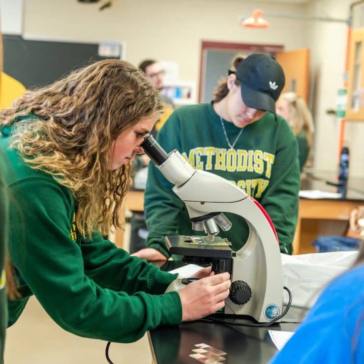 Methodist University students look into a microscope in Biology class.