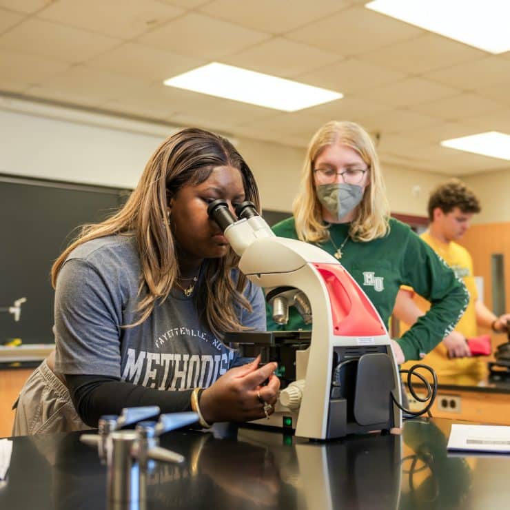 Methodist University Biology students look into a microscope together.