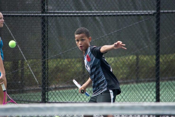 A youth takes a swing at a tennis ball with his racquet