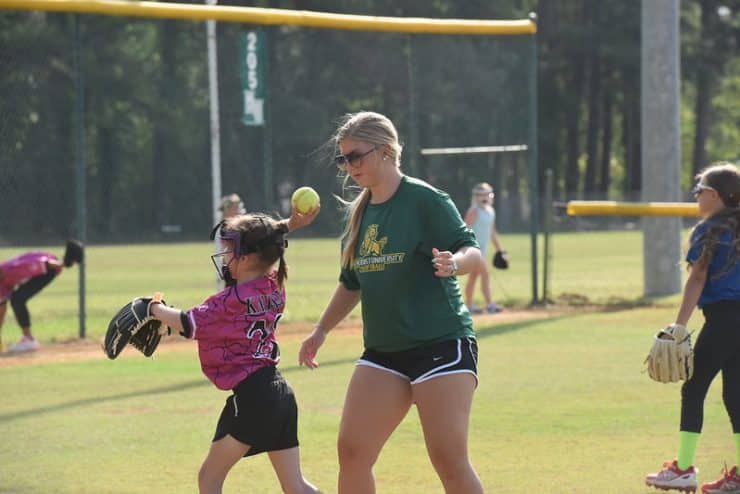 A camp counselor coaches a softball youth camp participant