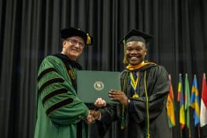 President Wearden stands with a student receiving their diploma during commencement.