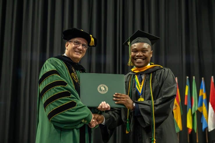 President Wearden stands with a student receiving their diploma during commencement.