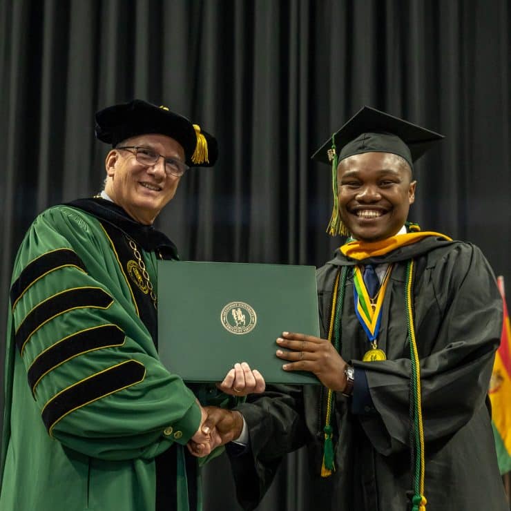 President Wearden stands with a student receiving their diploma during commencement.