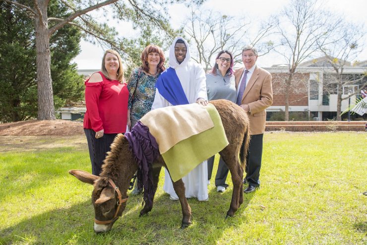 Faculty and Staff pose with a donkey for Holy Week