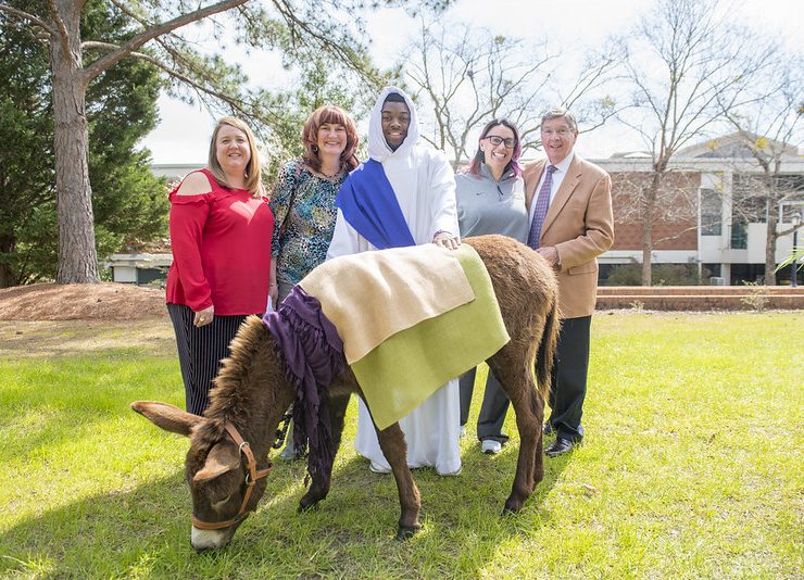 Faculty and Staff pose with a donkey for Holy Week