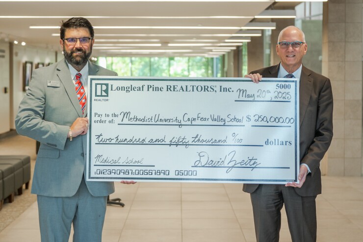 Methodist University President Stanley T. Wearden (right) accepts a symbolic check for the Methodist University Cape Fear Valley Health School of Medicine from David Zeitz, the interim president of The Longleaf Pine REALTORS® Association. 